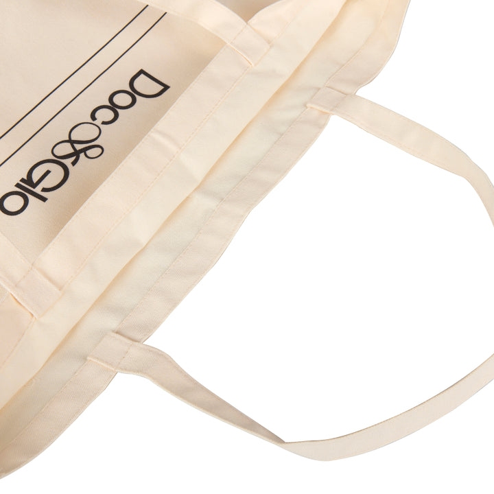Close-up of a beige tote bag with 'Doc ^ Glo' branding on a white background